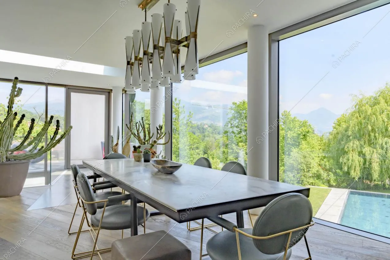 Tavolo da pranzo con lampadario di design nella sala con grandi vetrate con vista sul parco