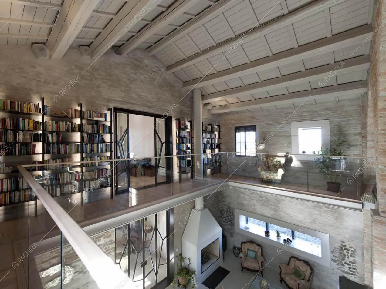 Soppalco con balaustra in vetro, libreria, soffitto intravi in legno a vista e camino