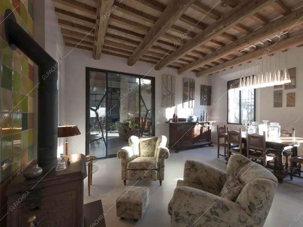 Sala con soffitto in travi in legno a vista, tavolo da pranzo e porta finestra con infissi neri