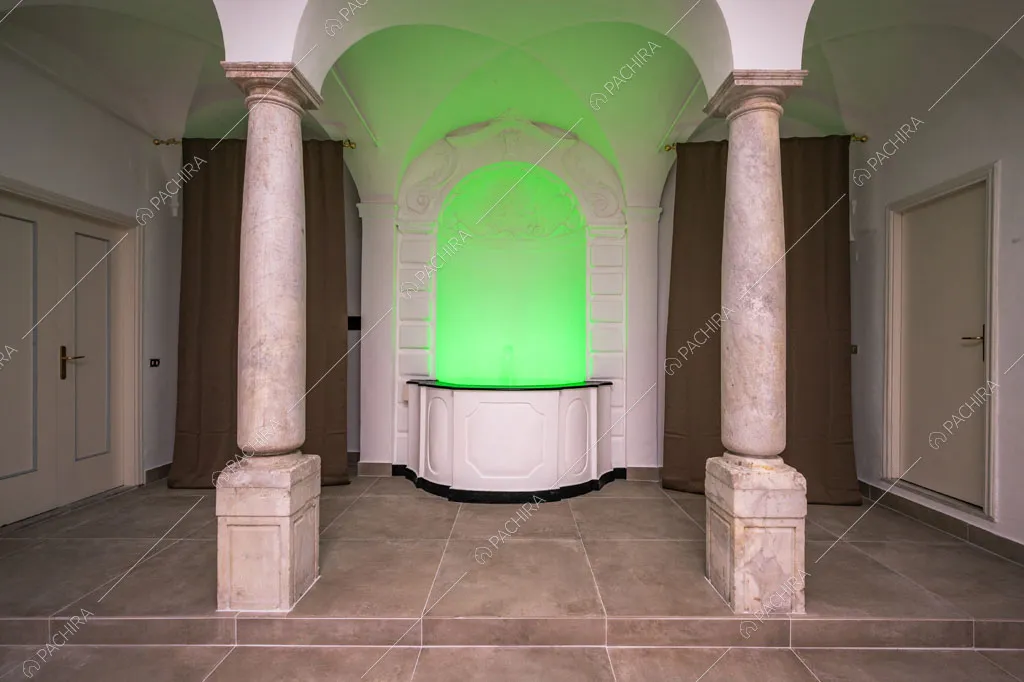 Fontana con boiserie e luce verde neon incorniciata da due colonne