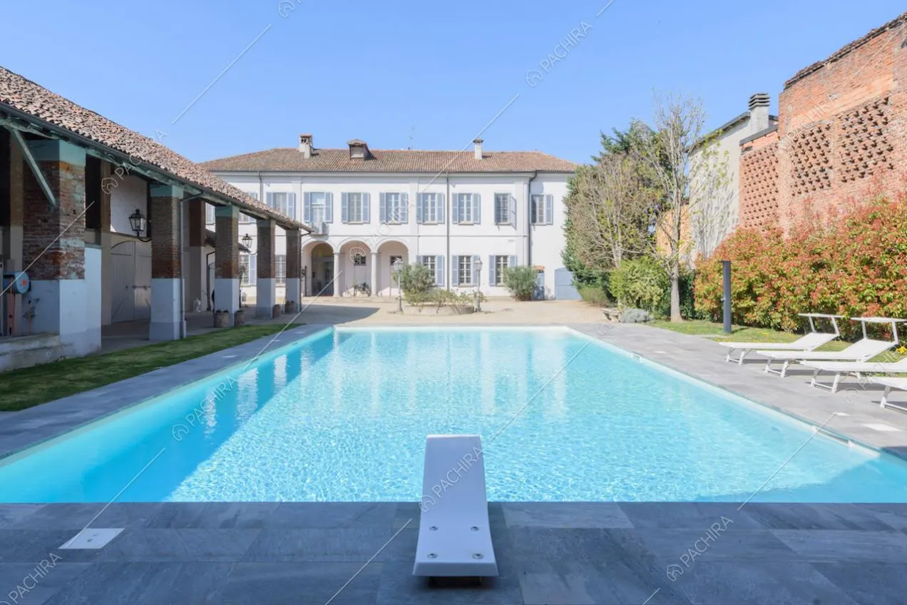 Grande piscina con trampolino e vista sulla struttura principale dagli esterni bianchi