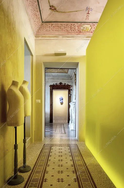 Lungo corridoio con manichini, soffitto affrescato e parete giallo fluo