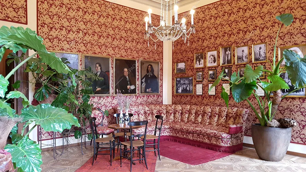 Salotto con arazzi e ritratti alle pareti, divano angolare e tavolo da pranzo