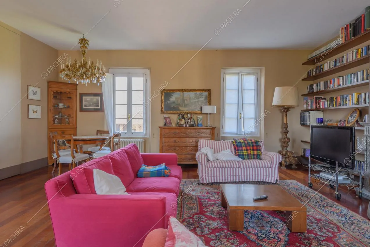 Divani fucsia, a righe, lampadario antico e pavimento in parquet nel salotto