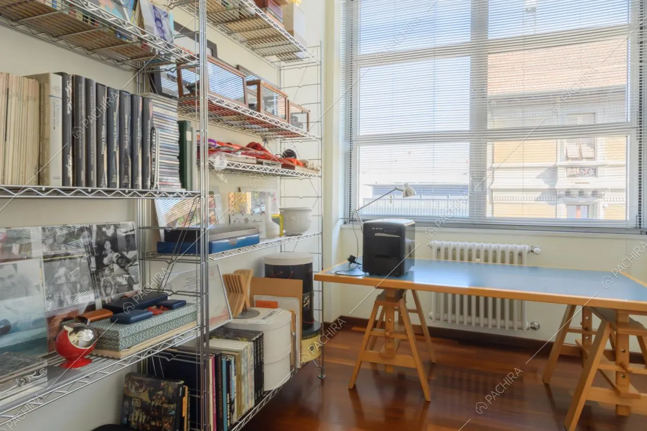 Luminoso studio con libreria in metallo, scrivania, pareti bianche e pavimento in parquet