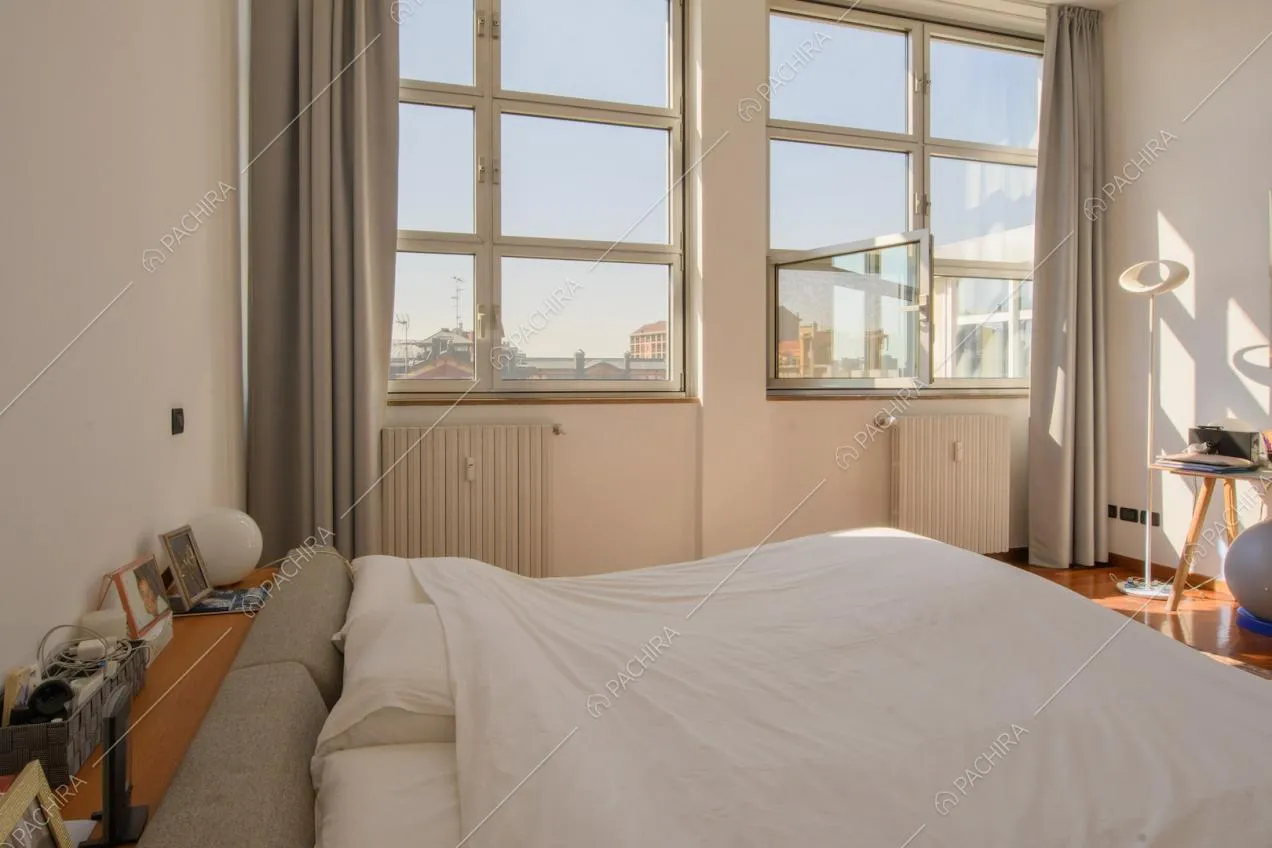 Letto matrimoniale nella luminosa camera con pavimento in parquet e pareti bianche