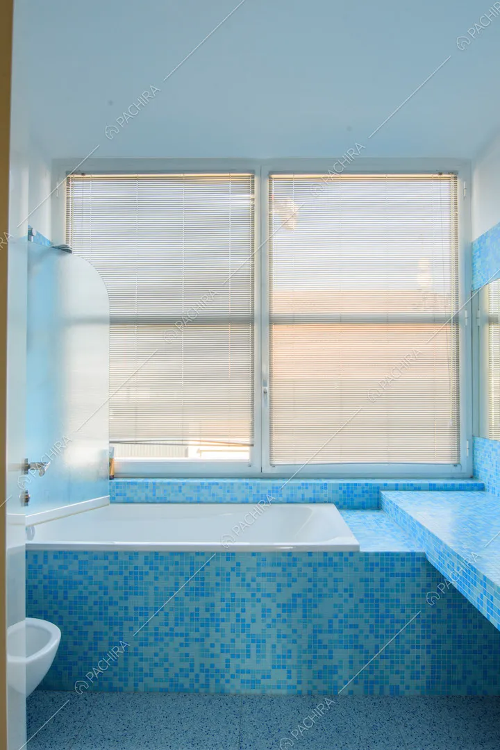 Luminoso bagno con vasca e piastrelline azzurre e blu su pavimento e pareti