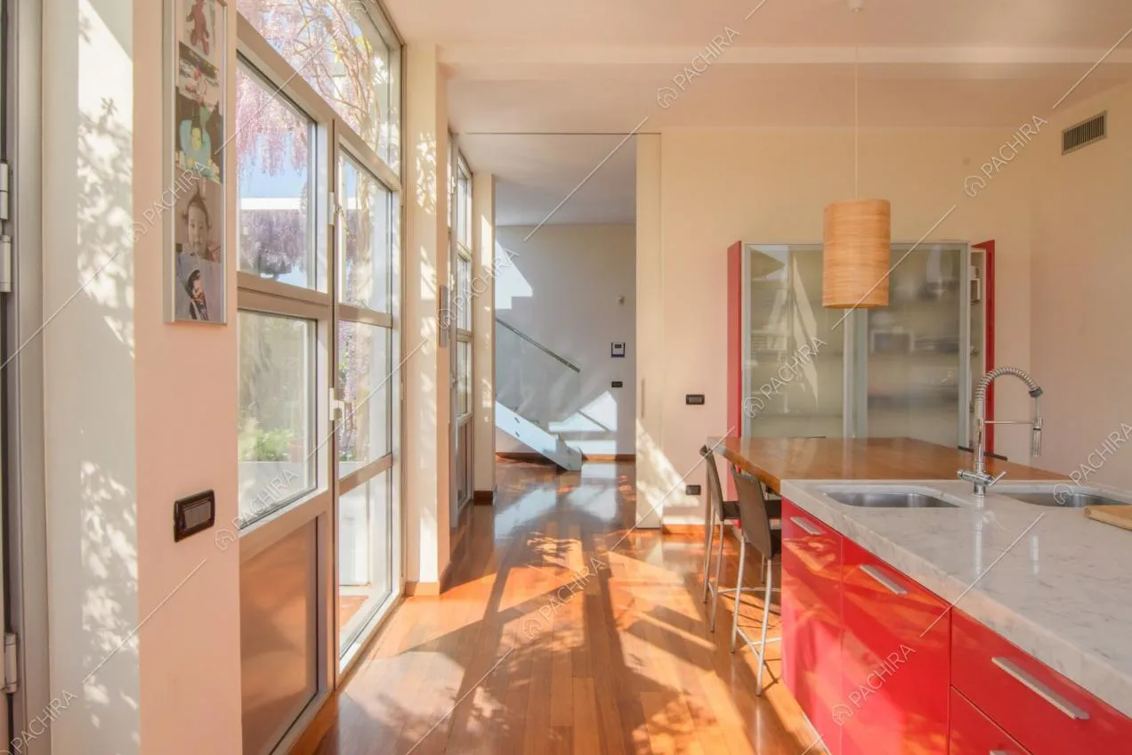 Pavimento in parquet nella cucina con isola rossa, vista sulle scale e vetrate