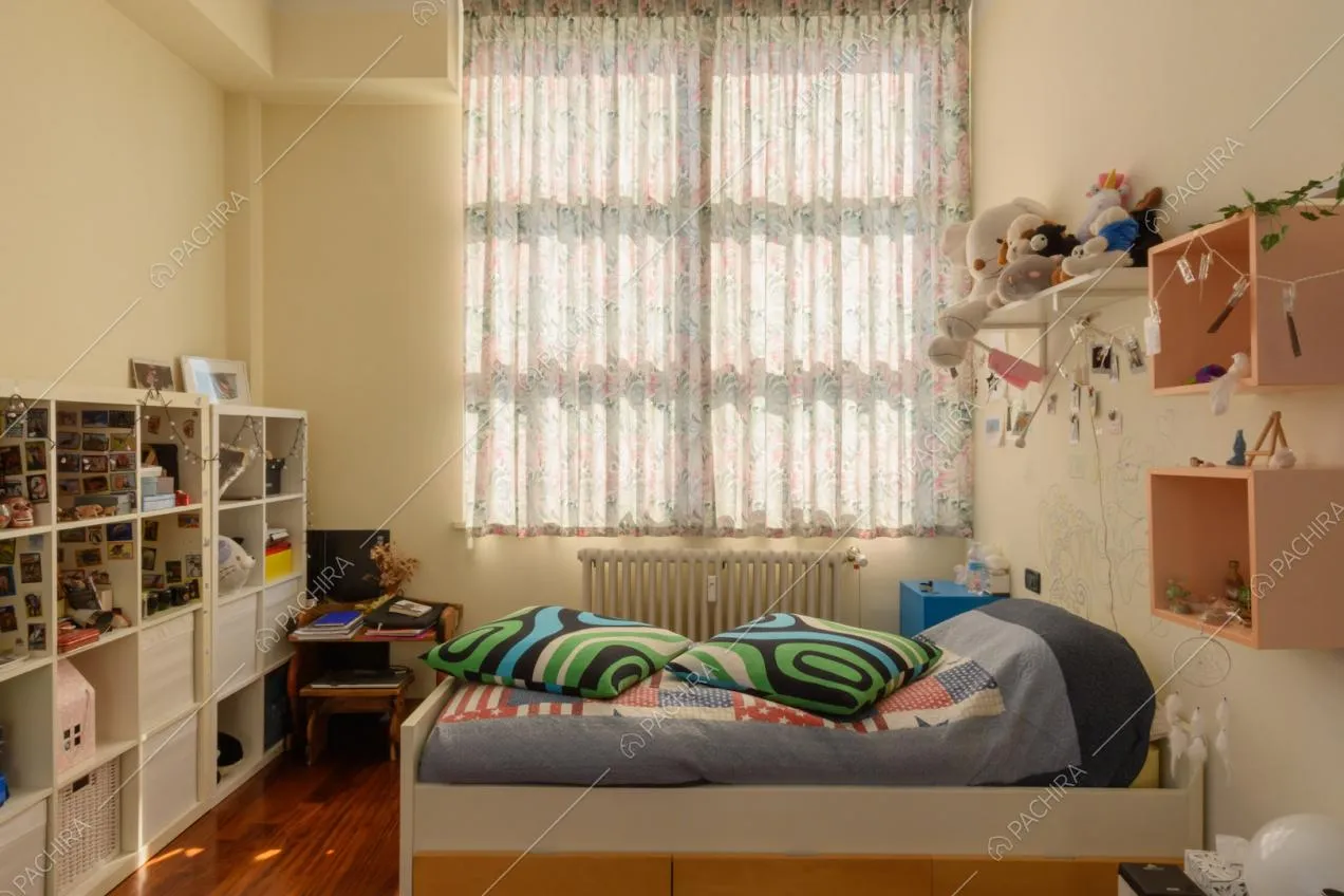 Letto singolo nella luminosa camera con pavimento in parquet, vetrate e libreria