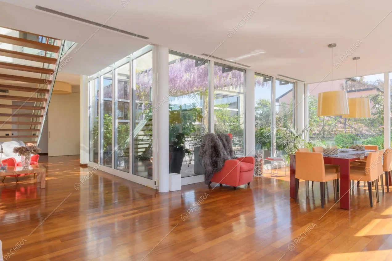 Zona living con vetrate, tavolo da pranzo rosso, scale e pavimento in parquet