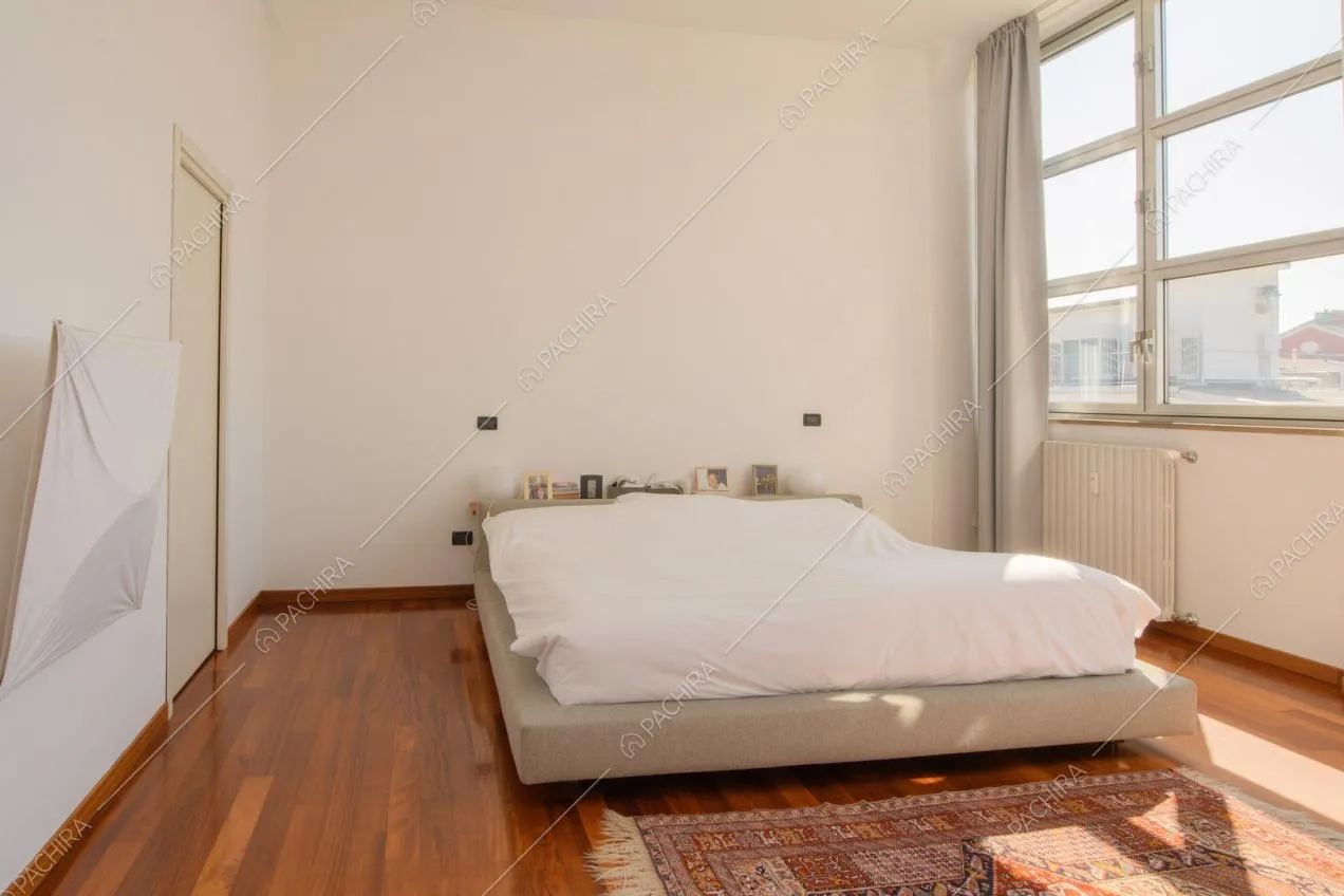 Camera da letto matrimoniale dalle pareti bianche con pavimento in parquet e vetrate