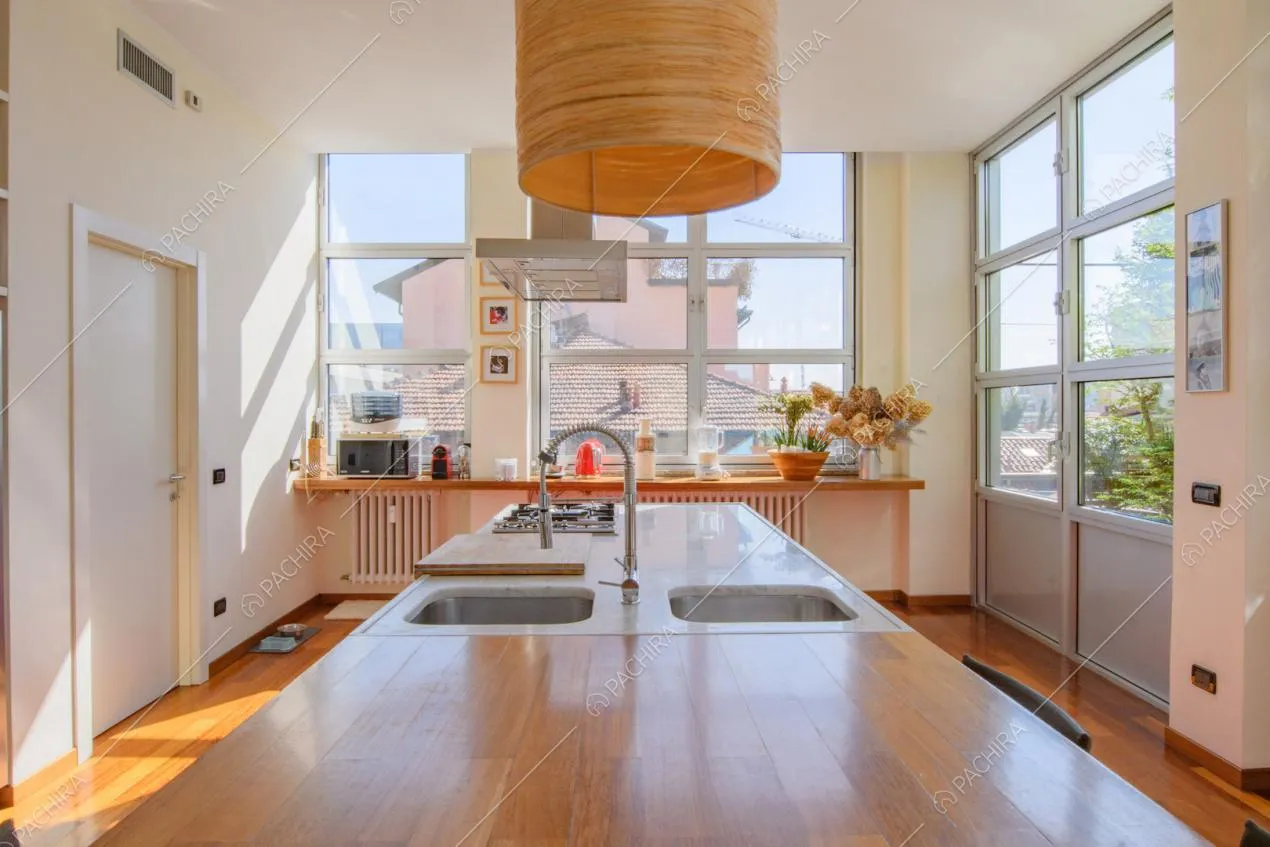 Isola in legno con doppio lavandino nella luminosa cucina con vetrate e pavimento in parquet