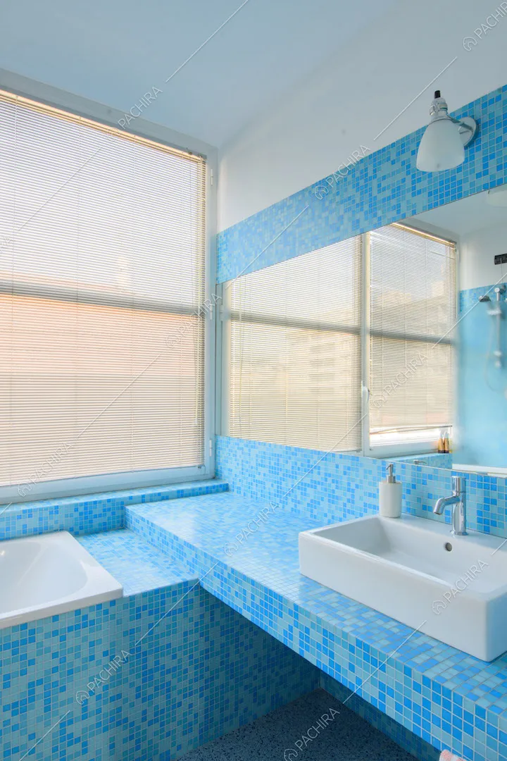 Piastrelline blu e azzurre nel luminoso bagno con vetrata e vasca