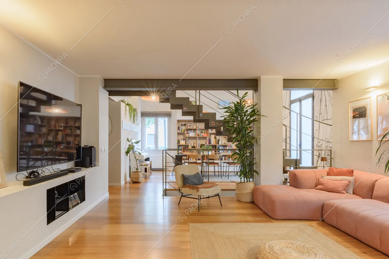 Luminoso salotto con divano rosa angolare, scale e pavimento in parquet