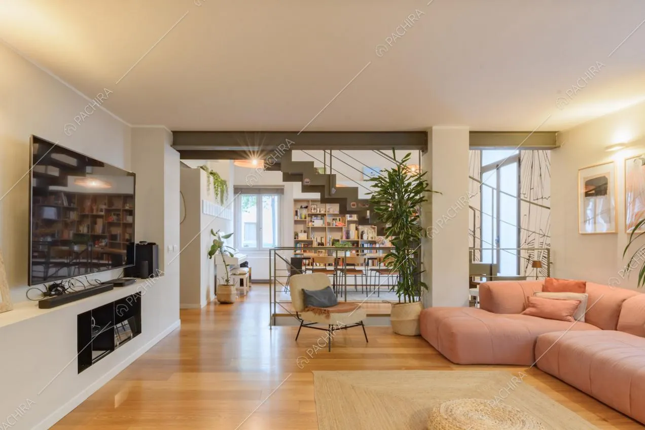 Luminoso salotto con divano rosa angolare, scale e pavimento in parquet
