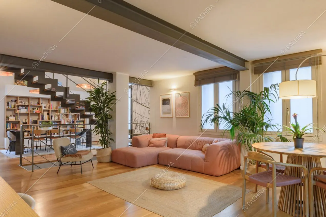 Divano angolare rosa, tavolo da pranzo in legno e vista sulla libreria