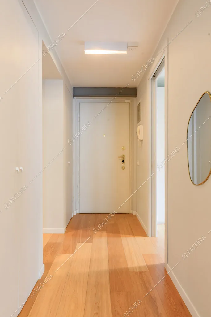 Dal corridoio con pareti bianche e pavimento in parquet vista sulla porta