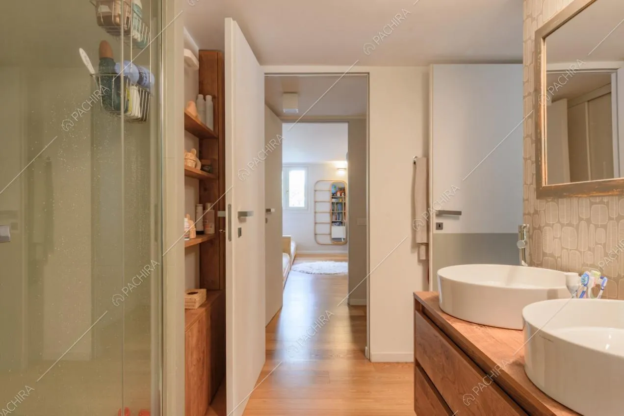Box doccia, doppio lavandino e carta da parati nel bagno con pavimento in parquet