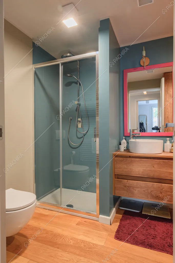 Bagno con pareti azzurre, box doccia e pavimento in parquet
