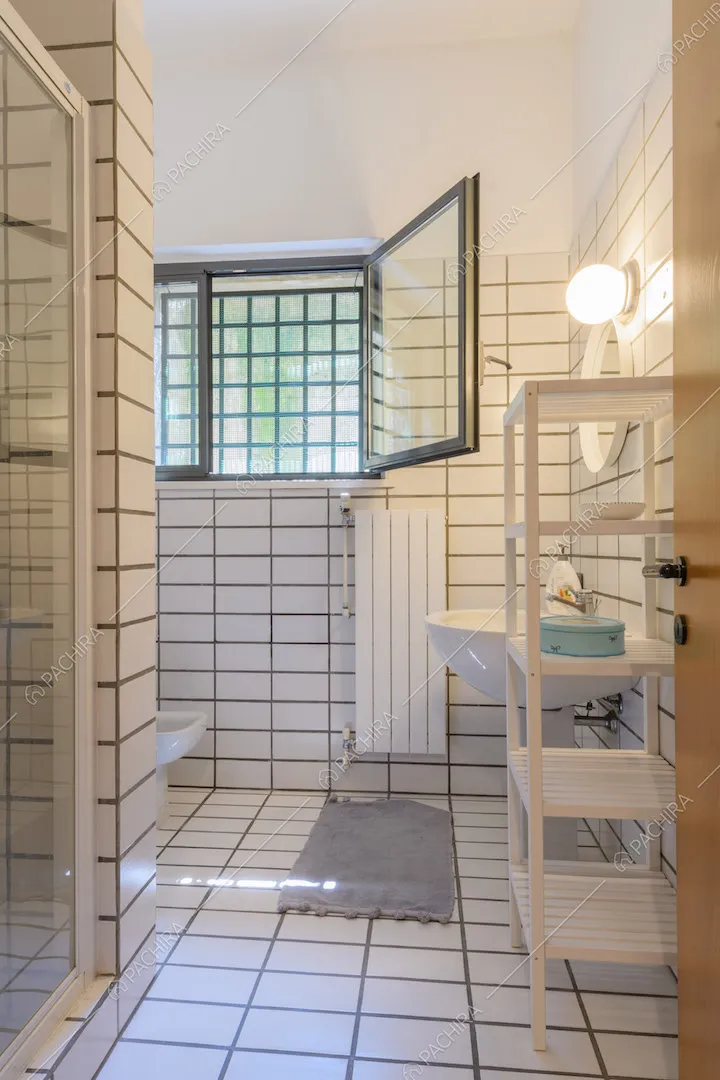 Bagno con pareti e pavimento in piastrelle bianche e box doccia
