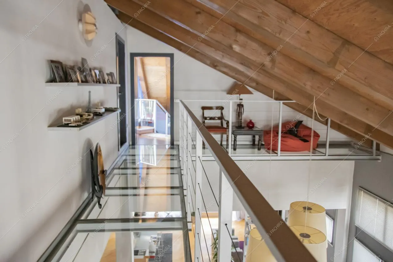 Balconata con pavimento in vetro, soffito con travi a vista in legno e vista sulle scale