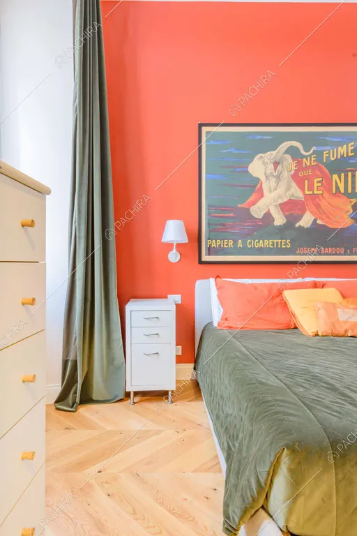 Parete rossa nella luminosa camera da letto con pavimento in parquet a spina di pesce