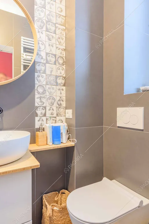 Bagno privato con piastrelle grigie e con le facce di Fornasetti