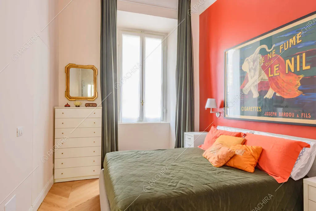 Letto matrimoniale nella luminosa camera con parete rossa e tende verdi