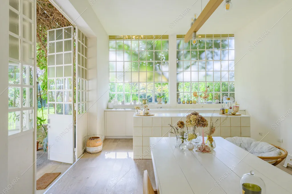 Tavolo da pranzo bianco, pavimento in parquet e grandi vetrate che riempiono di luce naturale la zona livingc