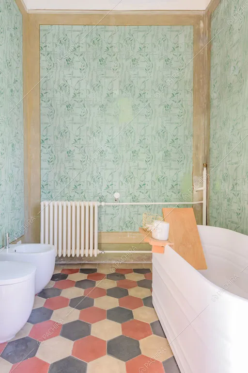 Vasca nel bagno con pavimento con cementine colorate e pareti con fantasia floreale verde