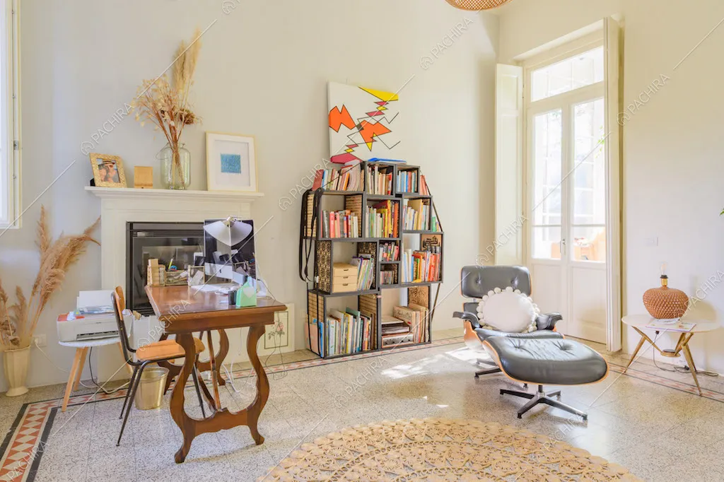 Luminoso salotto con libreria, poltrona di design, pareti bianche e porta-finestra