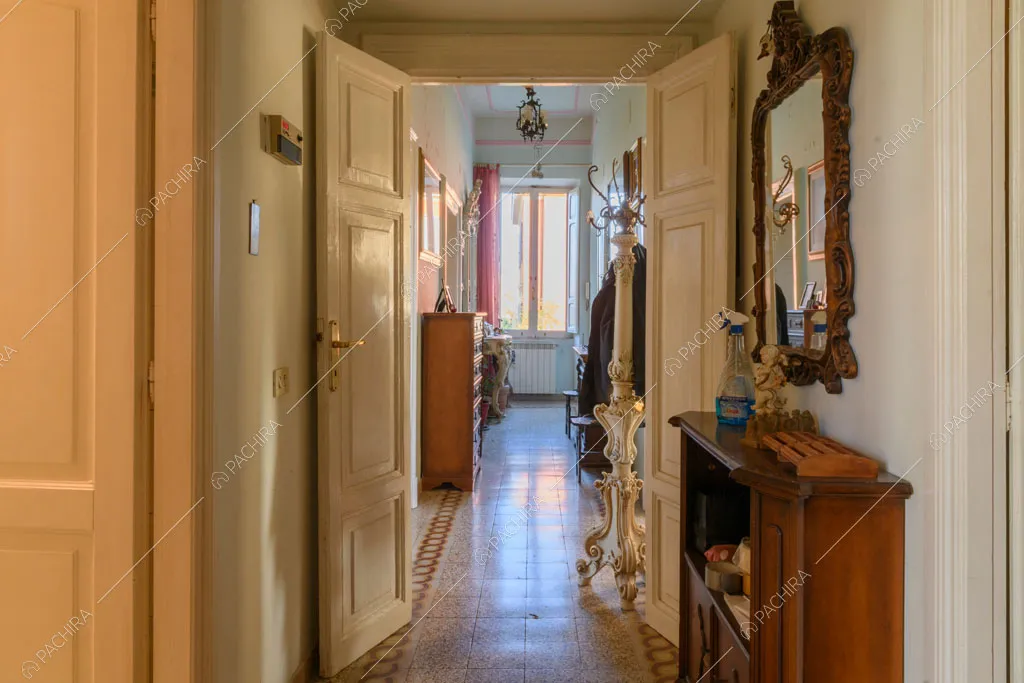 Lungo corridoio con porta bianca con boiserie e pavimento in graniglia