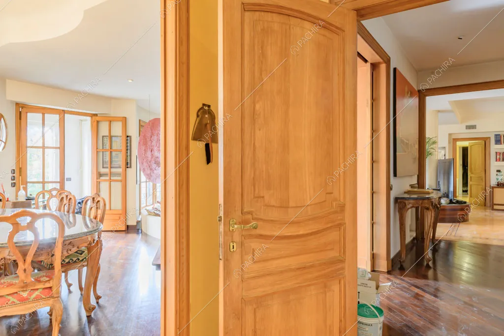 Porta con boiserie, scorcio sulla sala con tavolo da pranzo e sul corridoio
