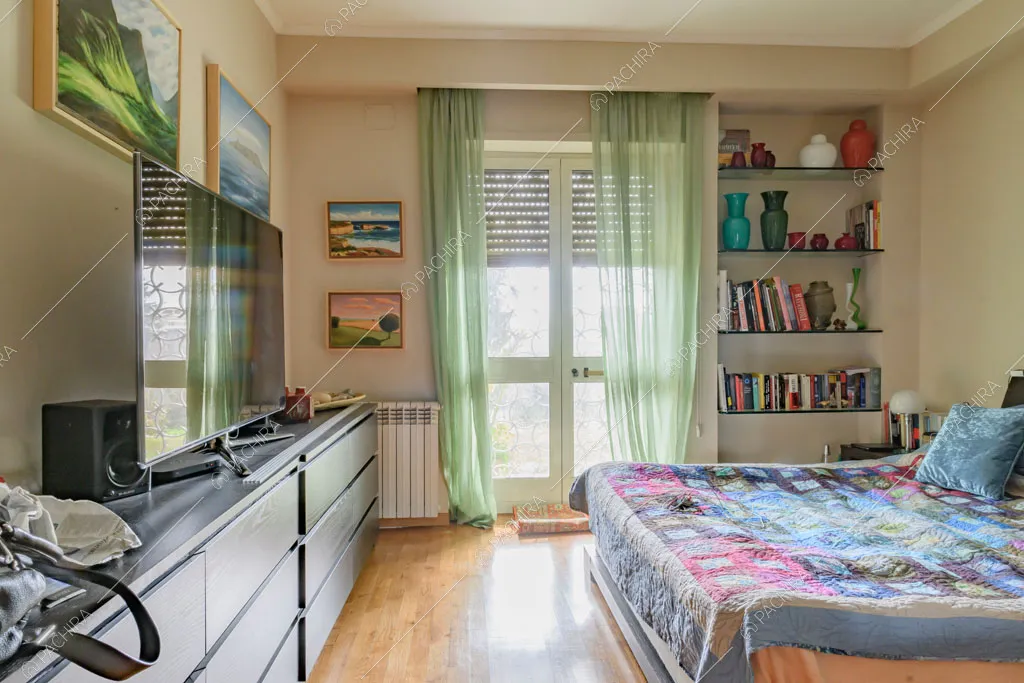 Camera da letto matrimoniale con pavimento in parquet, porte-finestre e tende verdi