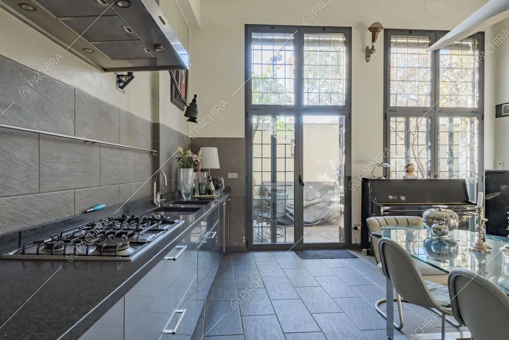 Cucina a parete con piano da lavoro nero, fornelli a gas e vista sul cortile tramite le porte-finestre