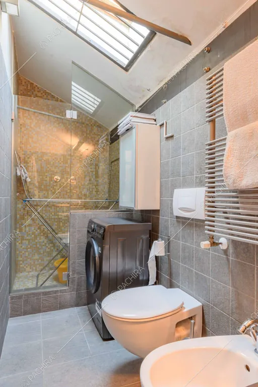 Bagno con pavimento e pareti in piastrelle grigie, box doccia e lucernario