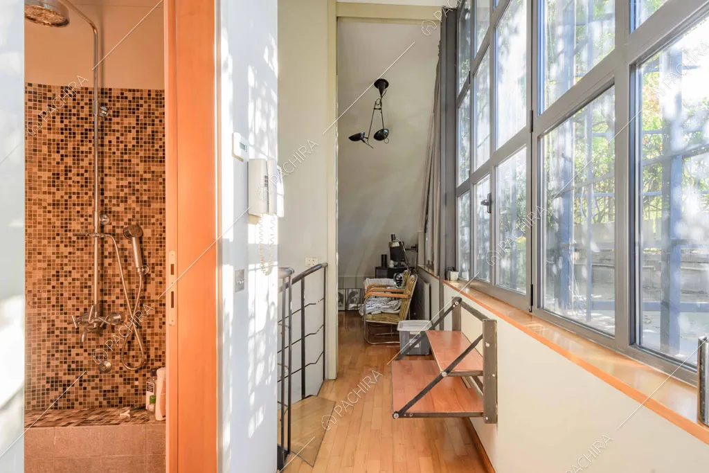 Luminoso corridoio con pavimento in parquet, vetrate in stile industriale e scorcio sul bagno