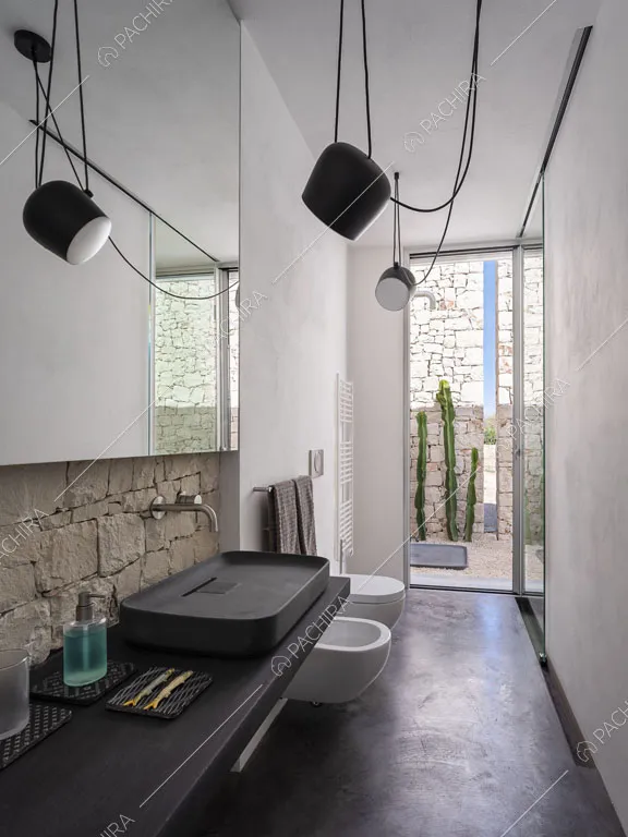 Pareti bianche, faretti e pavimento nero nel luminoso bagno con sanitari sospesi