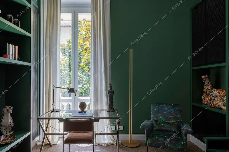 Studio con pareti verde scuro, scrivania e porta-finestra per accedere al balcone