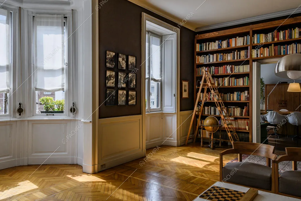 Bow window con boiserie nella luminosa sala con libreria a tutta parete e scorcio sulla sala da pranzo