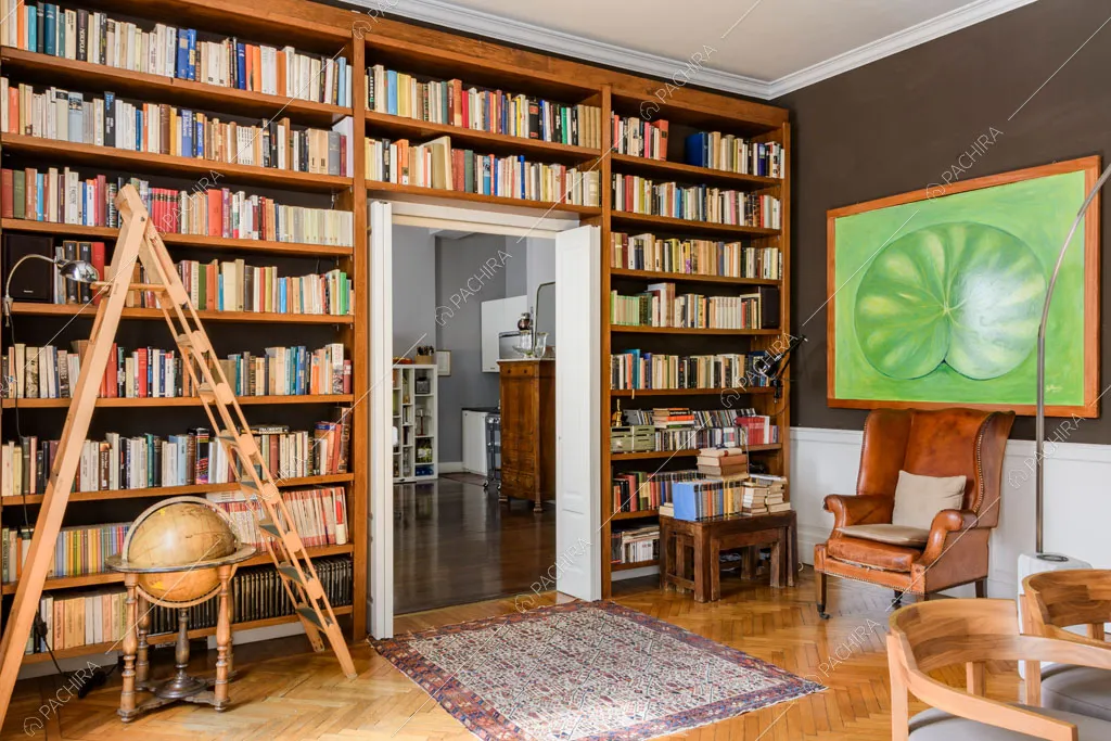 Libreria a tutta parete, poltrona antica in pelle e pavimento in parquet a spina di pesce nella sala