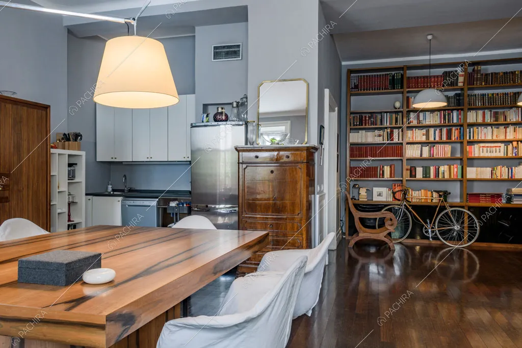 Sala da pranzo con cucina a parete a vista e libreria a tutta parete
