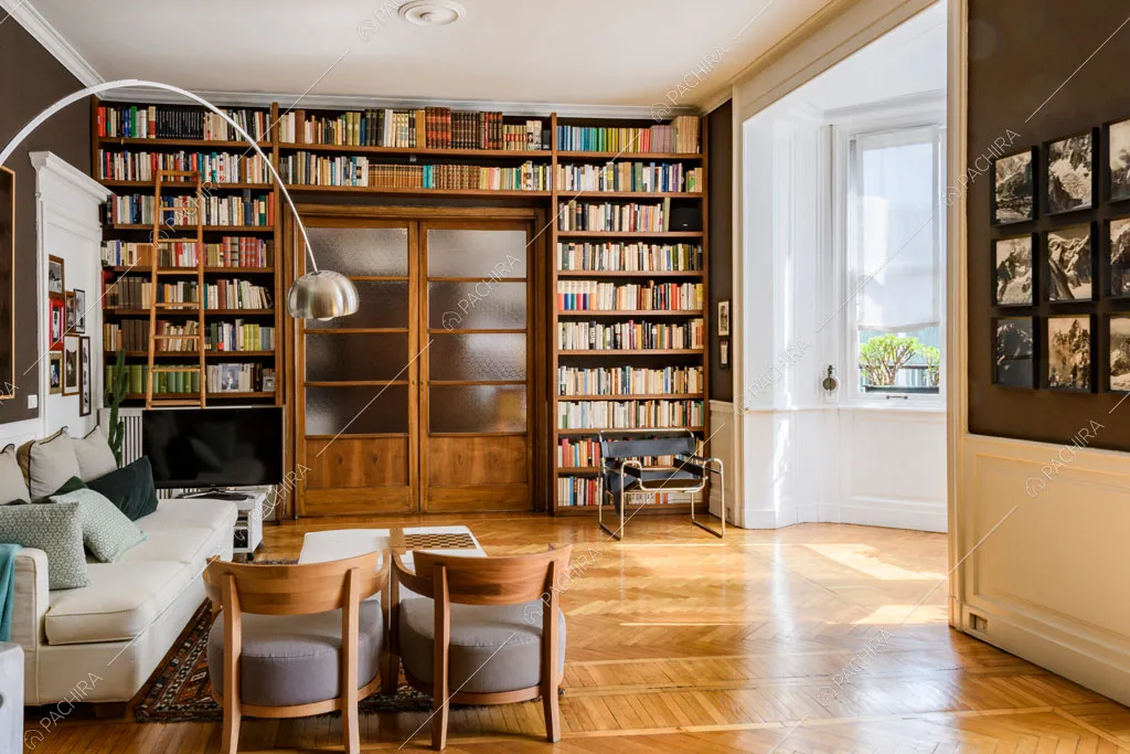 Pareti marroni e bianche con boiserie della luminosa sala con divano e pouf bianchi