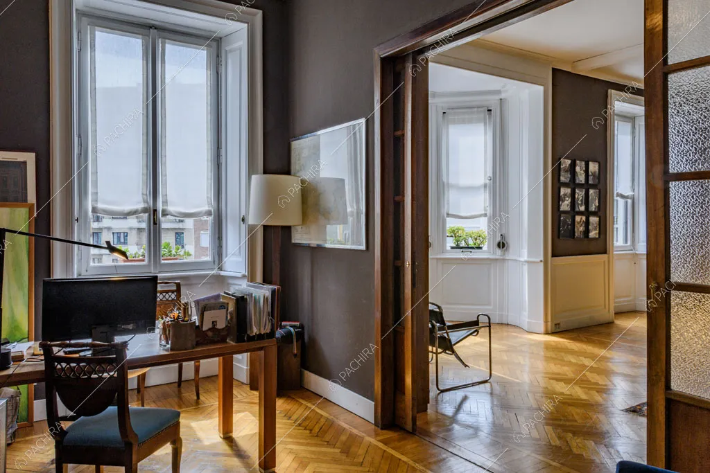 Studio con scrivania in legno, finestra con boiserie e scorcio sulla bow window della sala