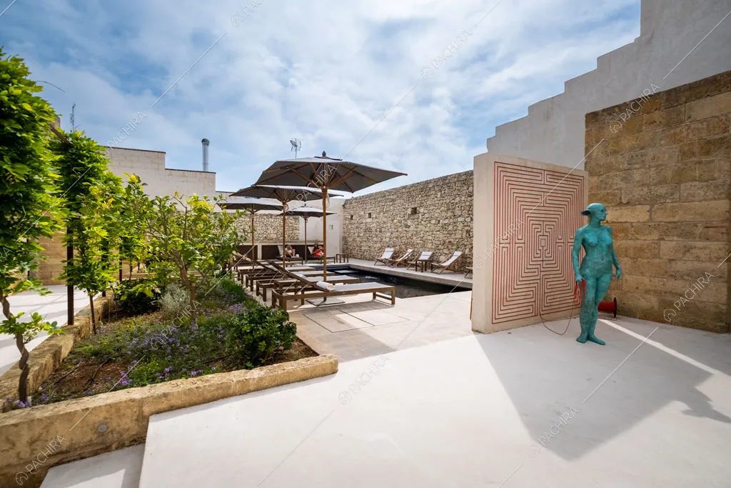 Grande giardino con piante, pietra a vista sul muro, piscina e opera d’arte
