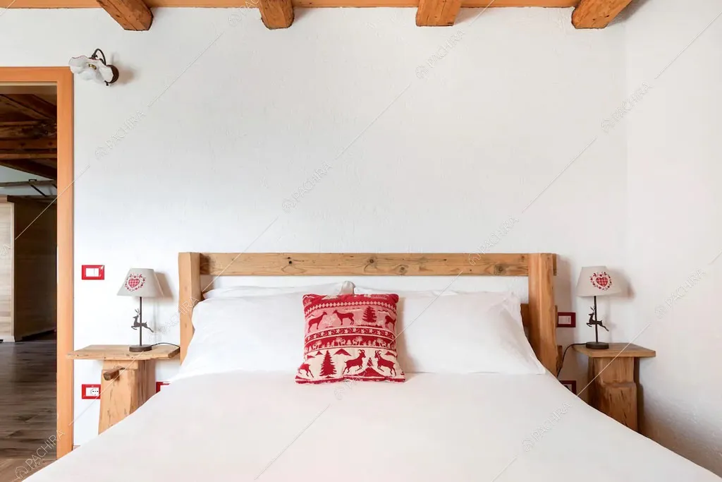 Letto matrimoniale nella camera con pareti bianche dello chalet Cantabrico, location in stile rustico a Trento