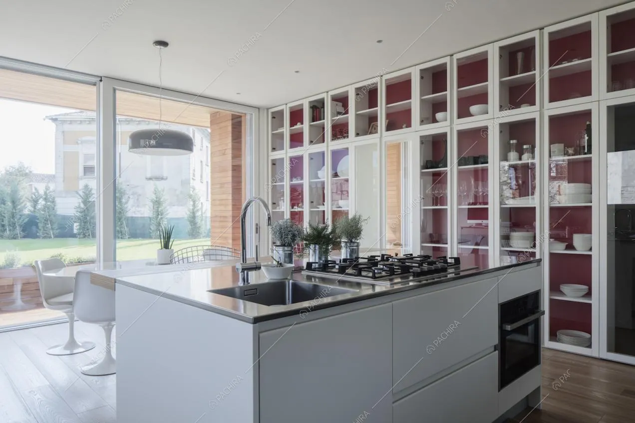 Isola bianca con lavandino e fornelli a gas nella cucina con la credenza a tutta parete in vetro