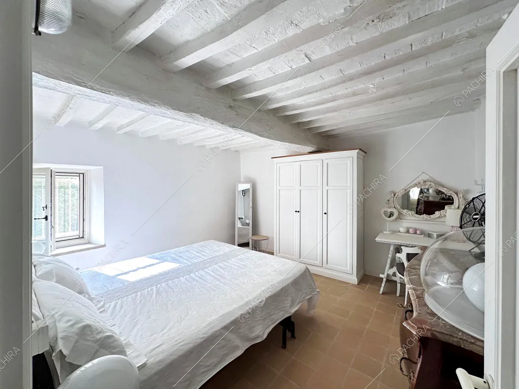 Letto matrimoniale nella camera con pareti bianche e travi a vista sul soffitto