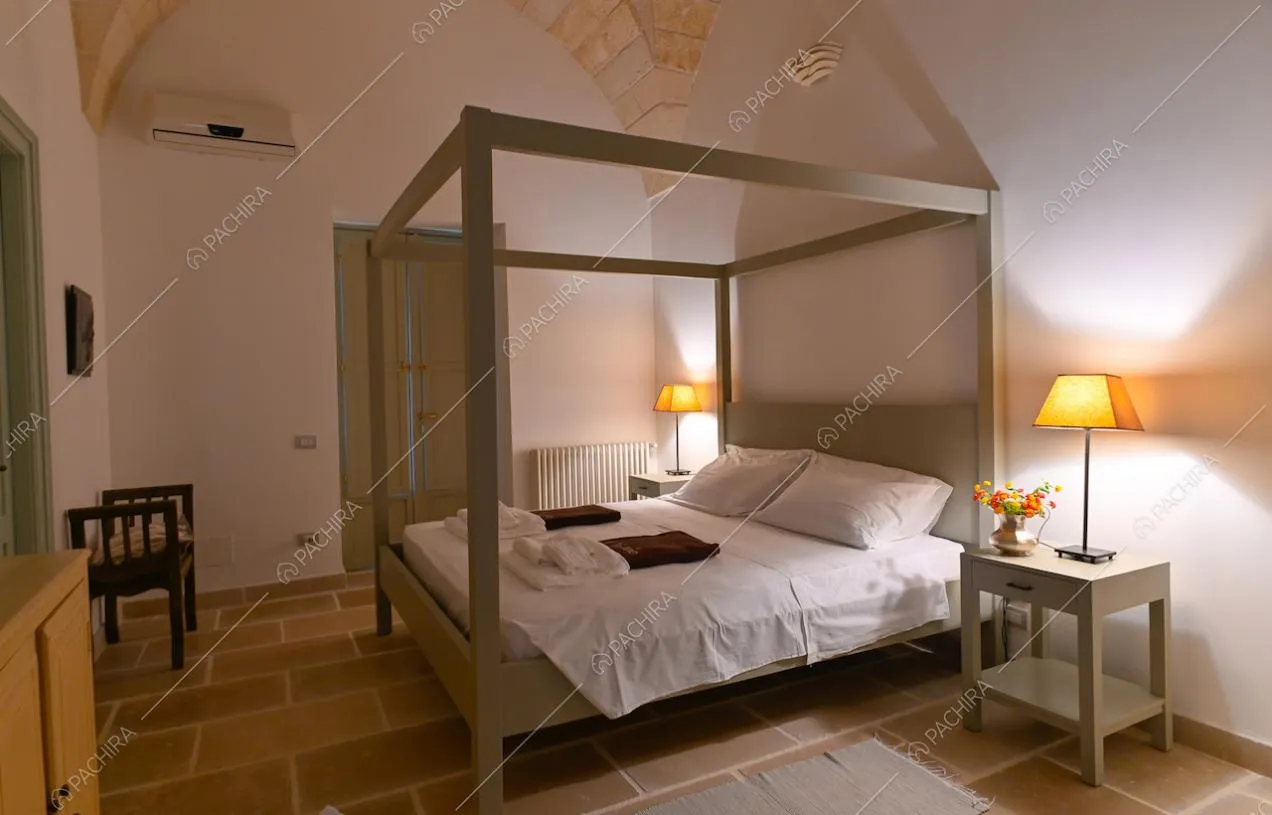 Camera matrimoniale con letto a baldacchino, pareti bianche e pavimento in pietra