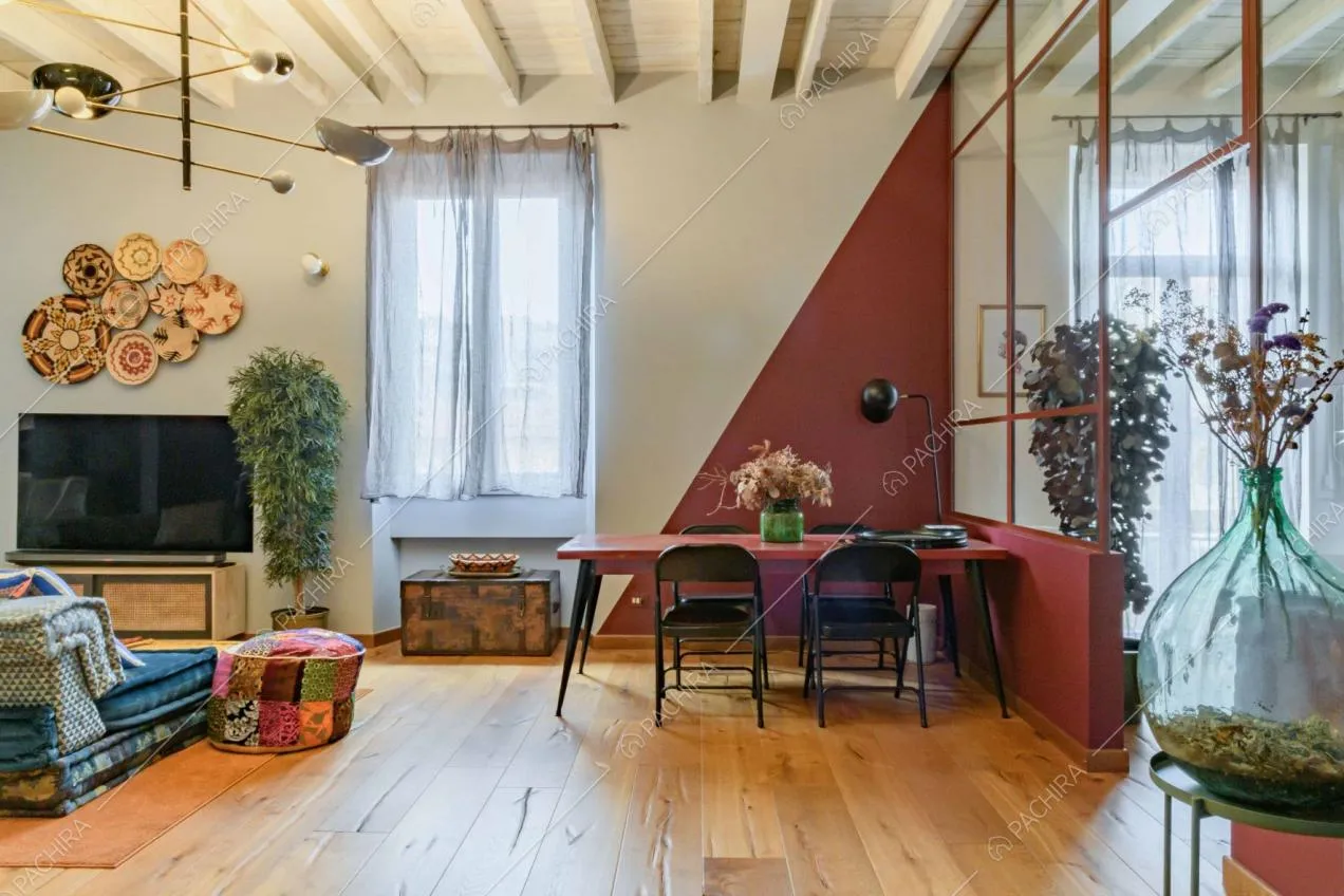 Tavolo da pranzo rosso nell'ampio e luminoso salone con vetrata in stile industrile che separa il salotto